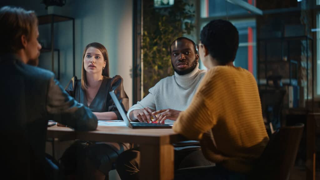 Tech Support Meeting, people discussing IT related topics around a table.